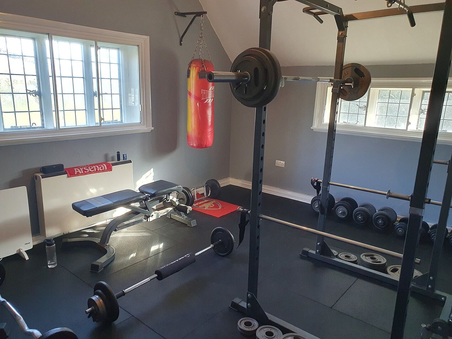 Black rubber tiles beneath a weight rack and bench in Chris’s home gym.