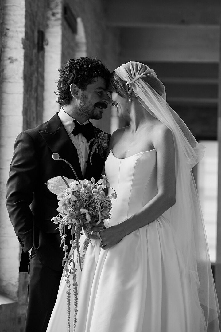 Phoebe and her husband forehead to forehead, her 1920s-style Zelda Juliet cap veil falling past her shoulders, her bouquet between them.
